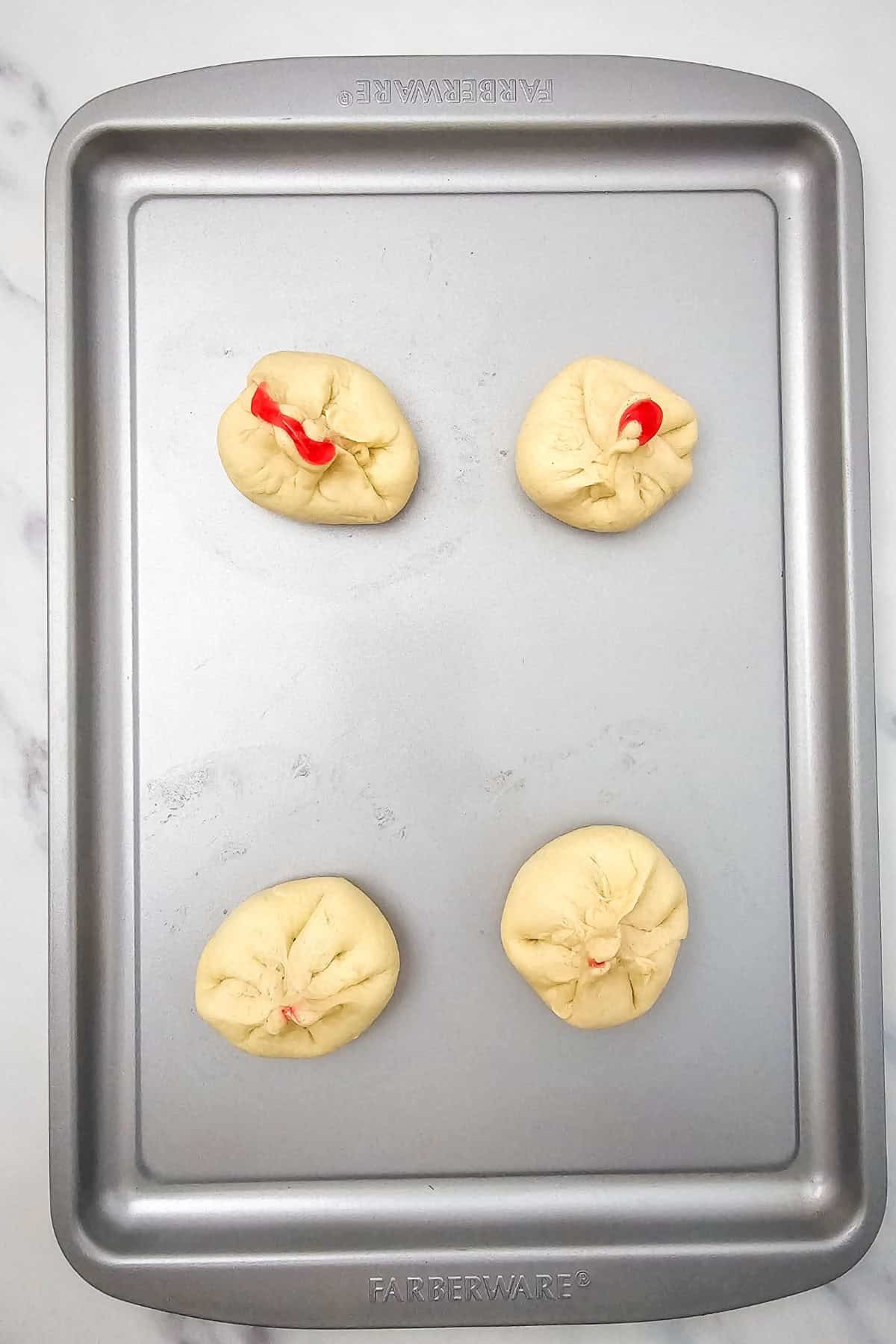 Biscuit dough being pinched at the edges to seal the cherry filling inside, forming a closed ball shape.