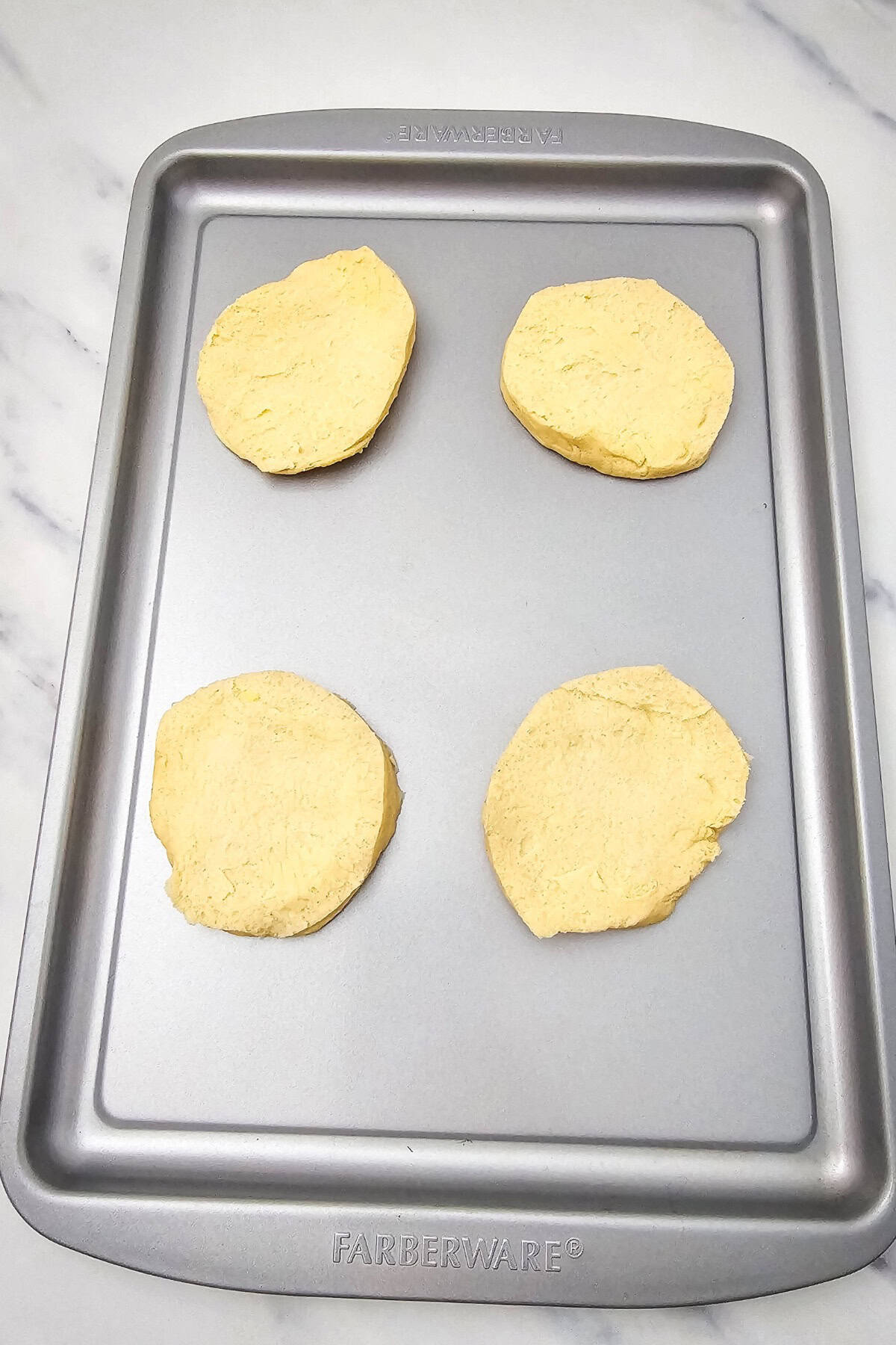 Unbaked biscuit dough pieces lined up evenly in the air fryer basket, ready to be filled.