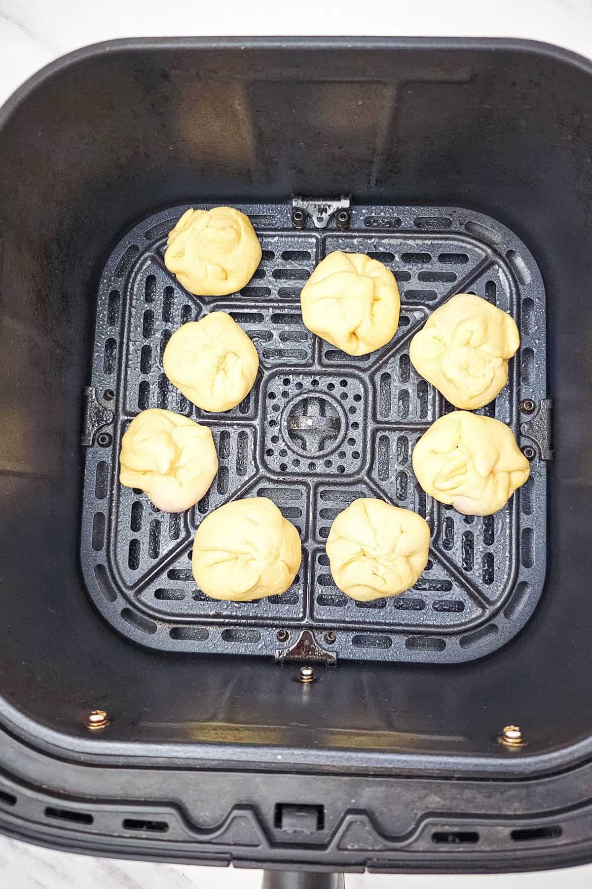 Filled biscuit placed in the air fryer basket, ready to cook, with others already positioned inside.
