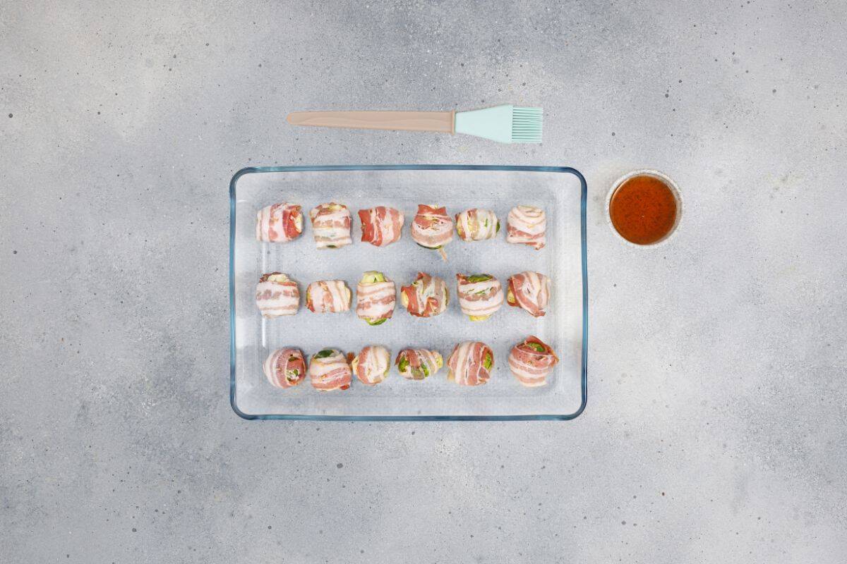 Bacon-wrapped Brussels sprouts neatly arranged on a serving dish with a small bowl of maple syrup on the side.