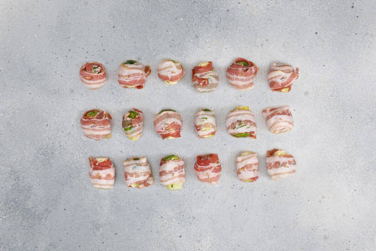 Bacon-wrapped Brussels sprouts neatly arranged on a flat surface, ready for baking.