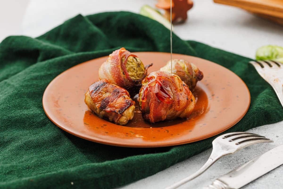 Maple-glazed bacon-wrapped Brussels sprouts served on a plate with green cloth underneath.