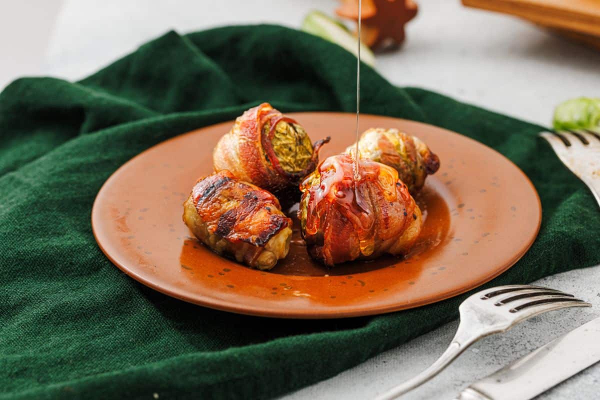 Maple-glazed bacon-wrapped Brussels sprouts served on a plate with green cloth underneath.