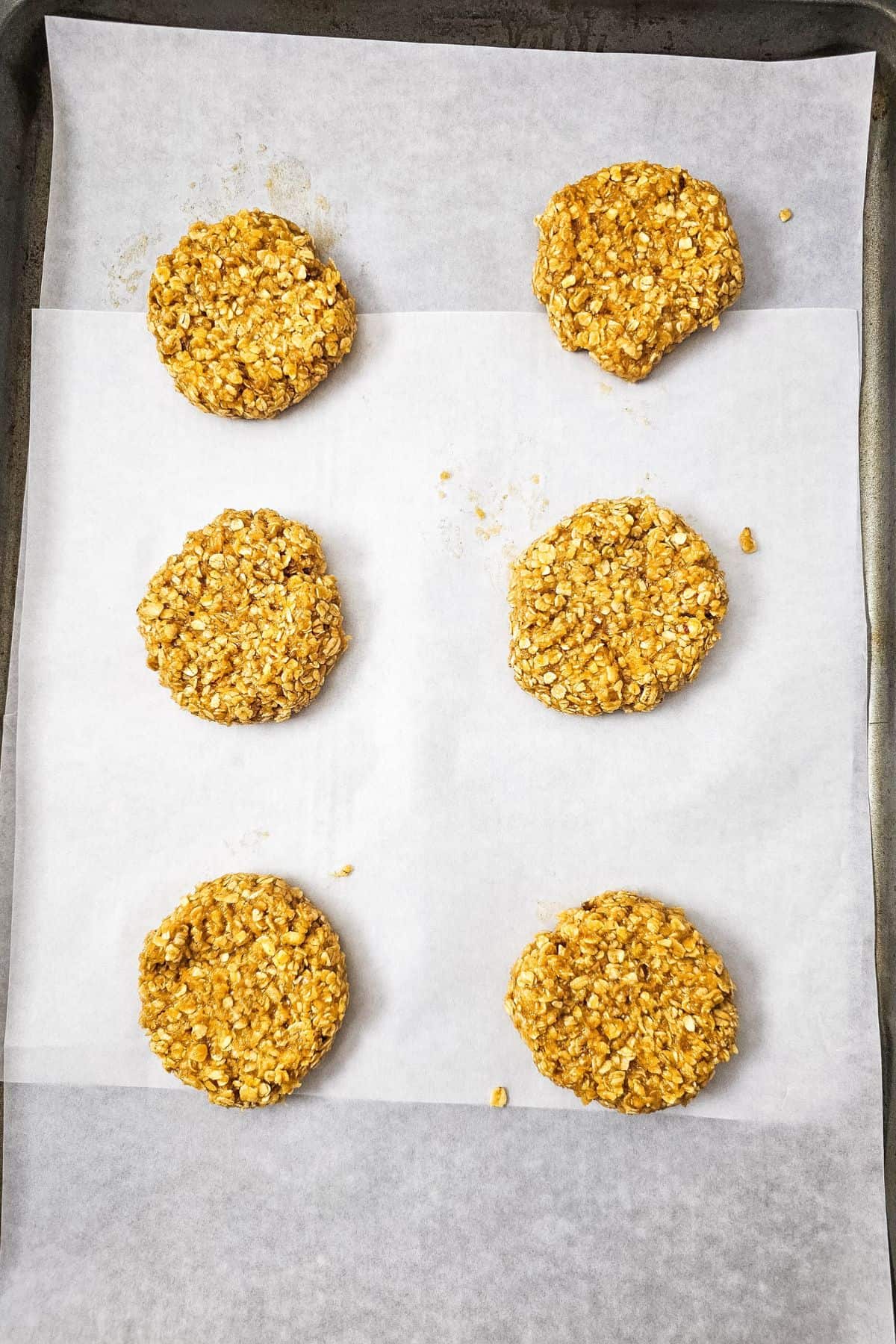 Cookie dough balls lined up on a parchment‑paper‑lined baking pan, ready to bake.