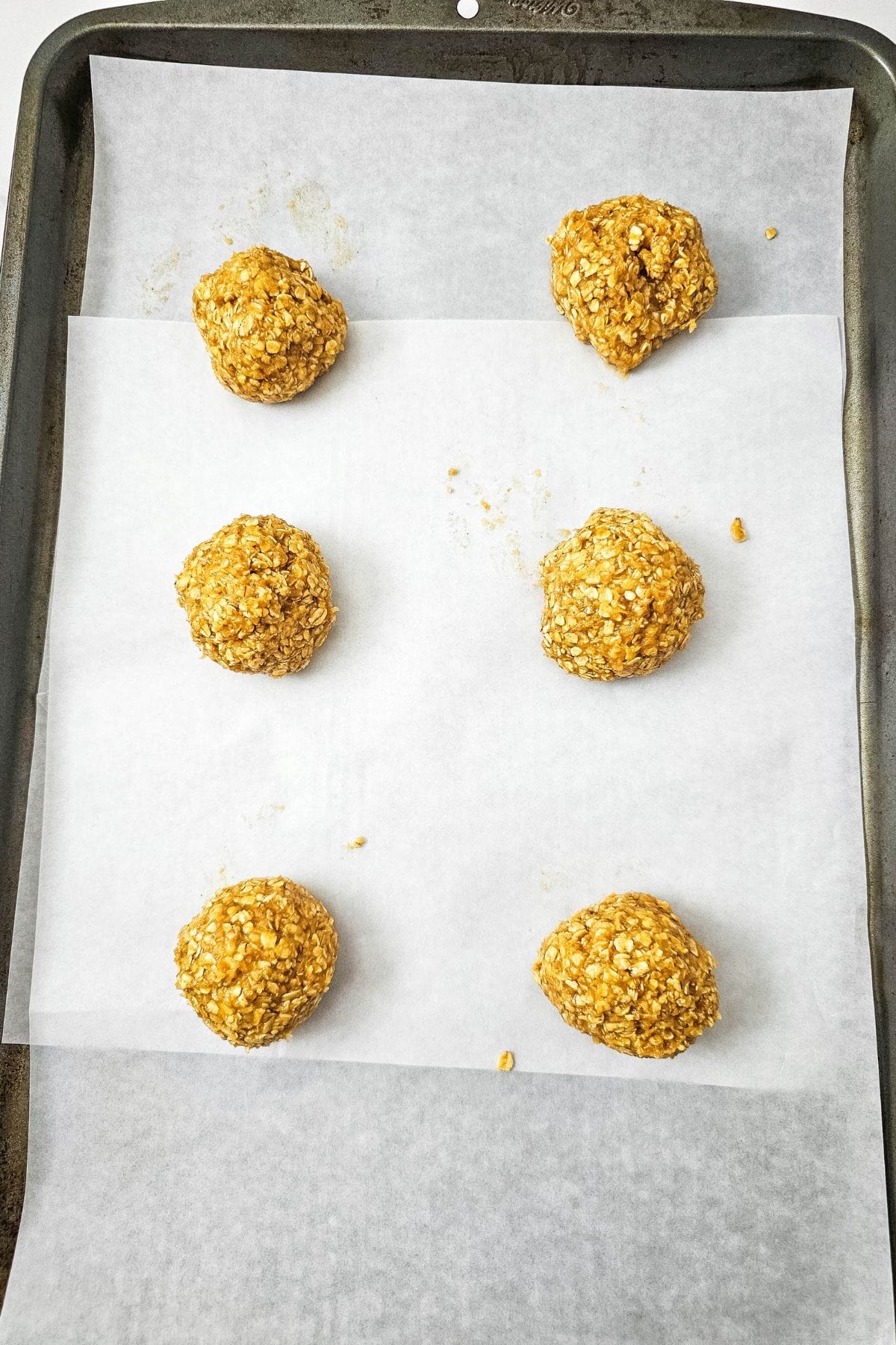 Rolled cookie dough balls lined up on a parchment‑paper‑lined baking pan, ready for baking.
