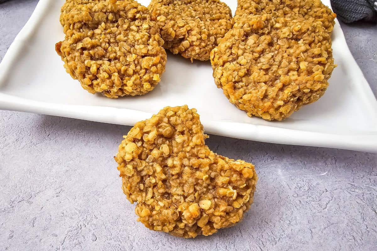 A bitten peanut butter oatmeal cookie with a few whole cookies in the background.