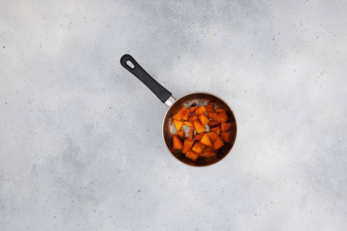 Pumpkin cubes, spinach, and crumbled feta being added to a saucepan.