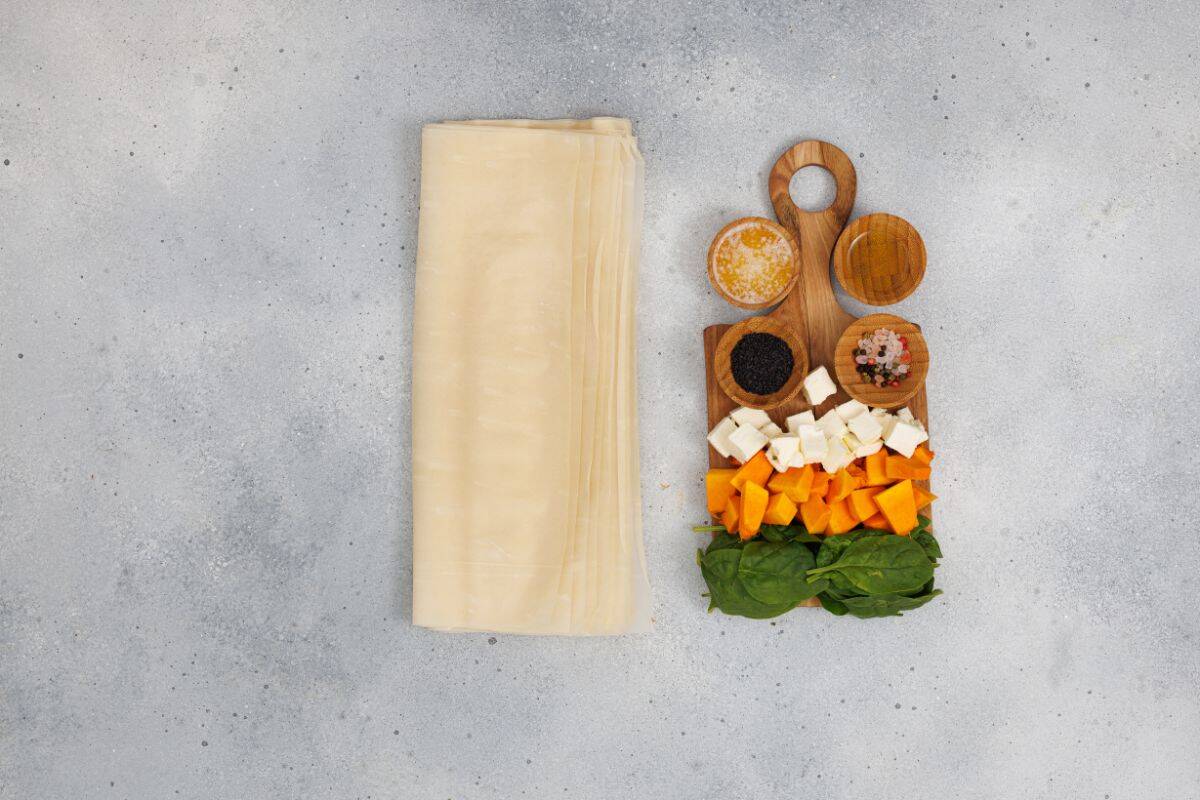 Thin sheets of phyllo dough and ingredients arranged neatly on a wooden board.