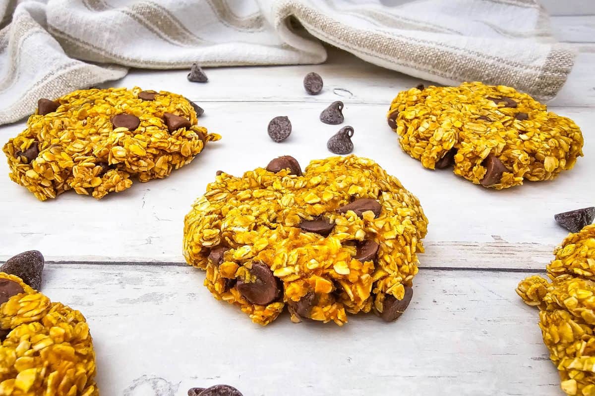 Freshly baked pumpkin oatmeal cookies surrounded by chocolate chips on a surface.