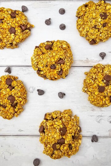Freshly baked pumpkin oatmeal cookies surrounded by chocolate chips on a surface.