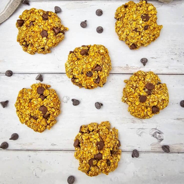Freshly baked pumpkin oatmeal cookies surrounded by chocolate chips on a surface.