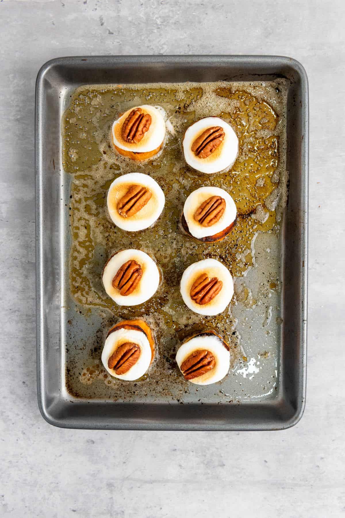 Sweet potato slices on a baking tray topped with marshmallows and pecans, ready to be baked.
