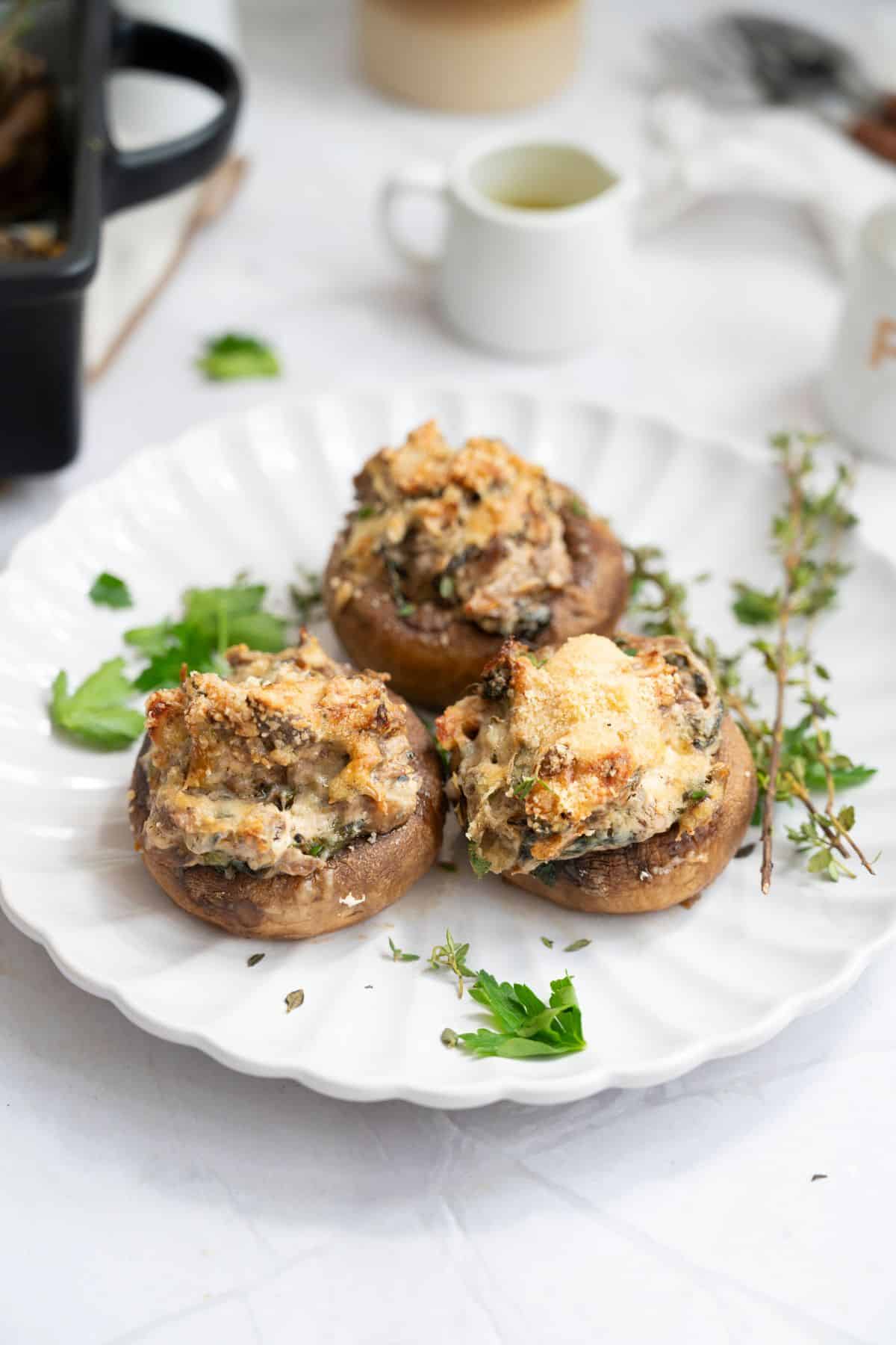 A plate with three stuffed mushrooms, garnished with fresh herbs.
