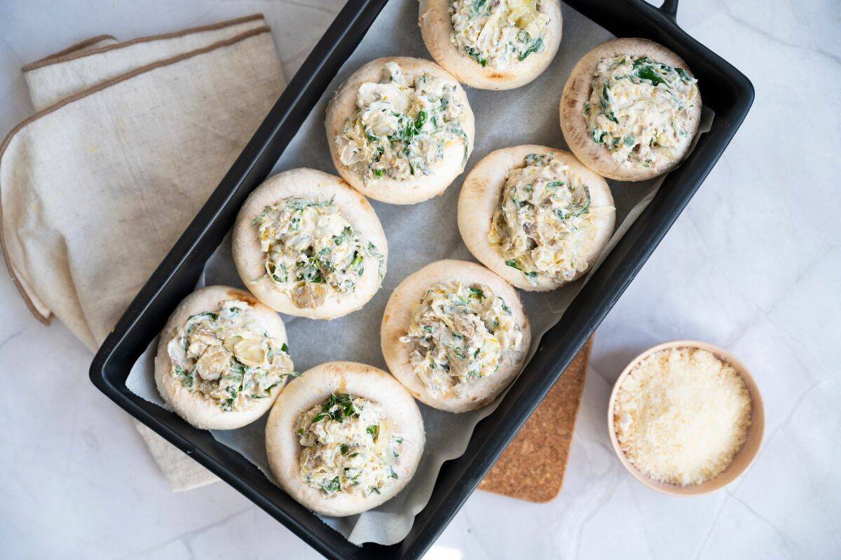 A serving dish with neatly arranged stuffed mushroom with cheese parmesan on the side.