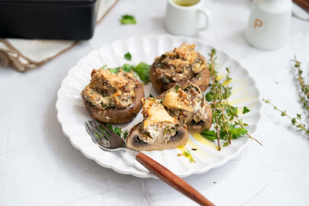 A plate with stuffed mushrooms, garnished with fresh herbs with fork on the side.
