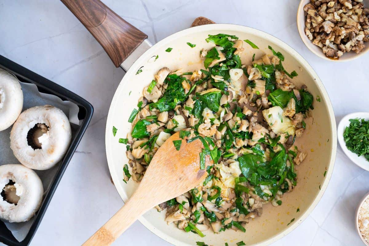 A spatula mixing the spinach, mushroom stems, and artichokes in a medium pan.