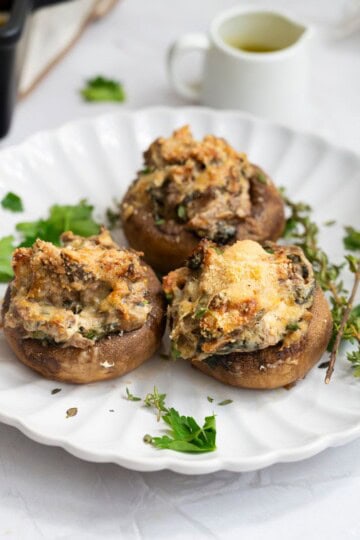 A plate with three stuffed mushrooms, garnished with fresh herbs.