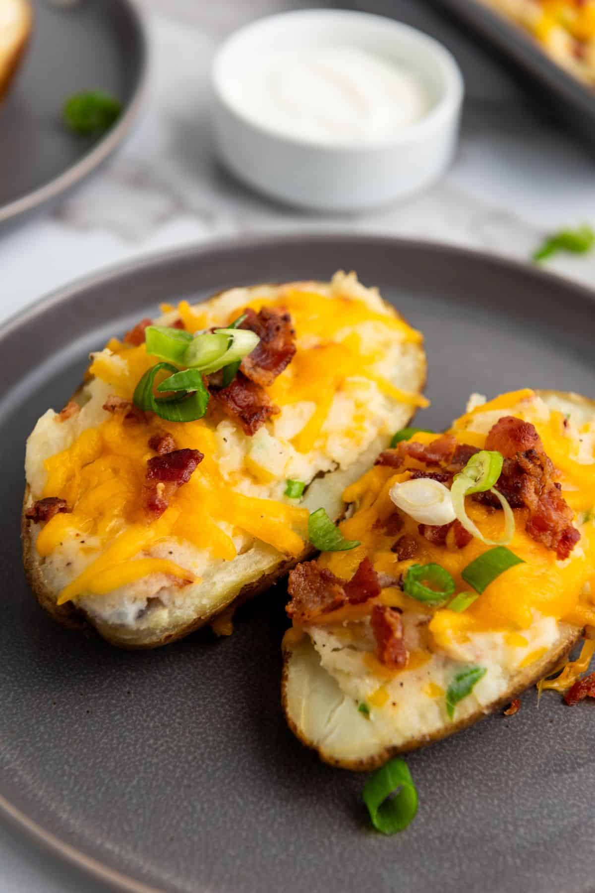 Two twice-baked potato halves served on a plate, topped with melted cheese, bacon bits, and sliced scallions.