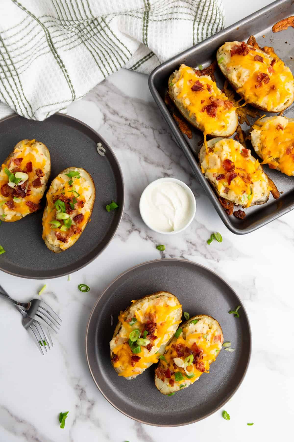 Several plates, each with two twice-baked potatoes topped with melted cheese, bacon, and scallions.