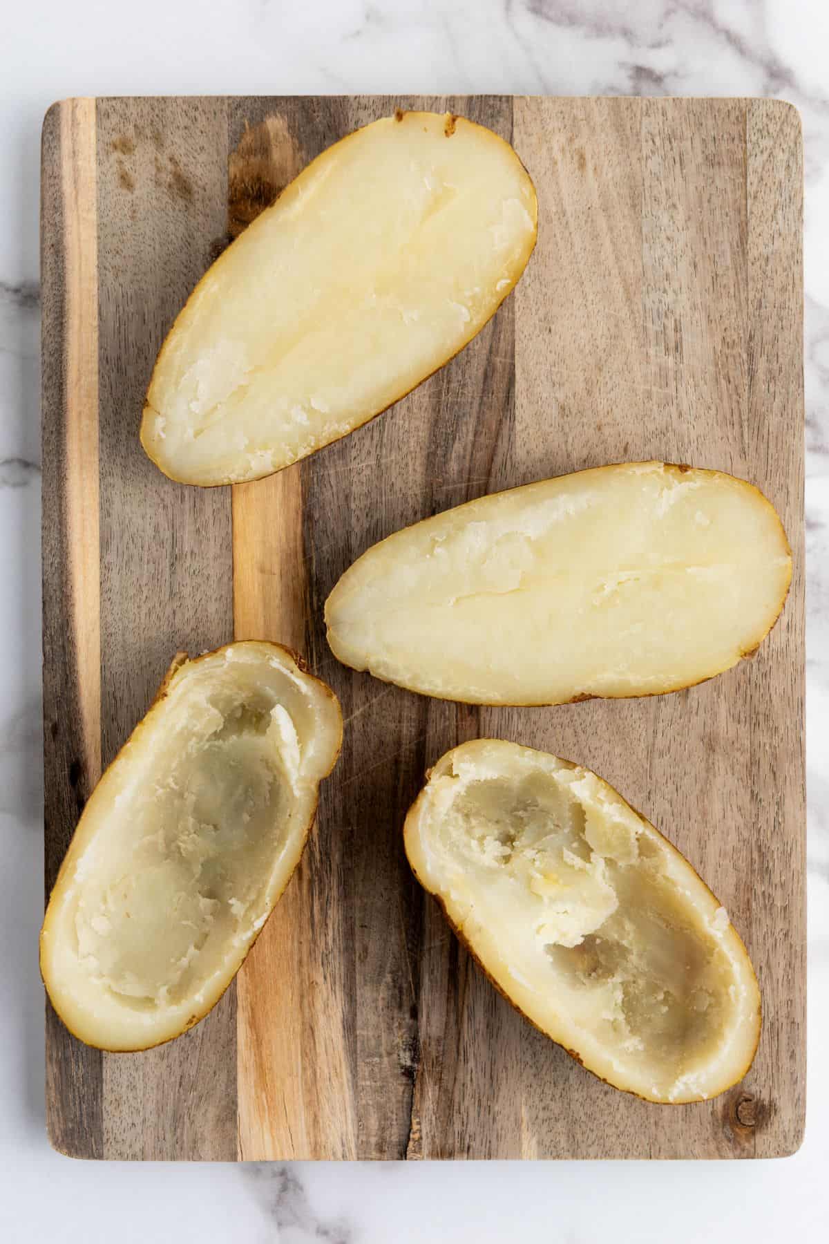 A baked potatoes sliced in half with the inside being scooped out using a spoon.