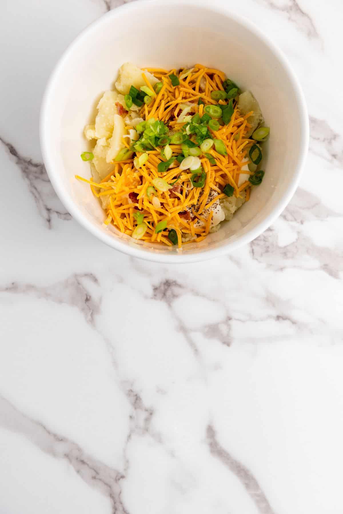 A bowl of mashed potato mixture with ingredients being mixed.