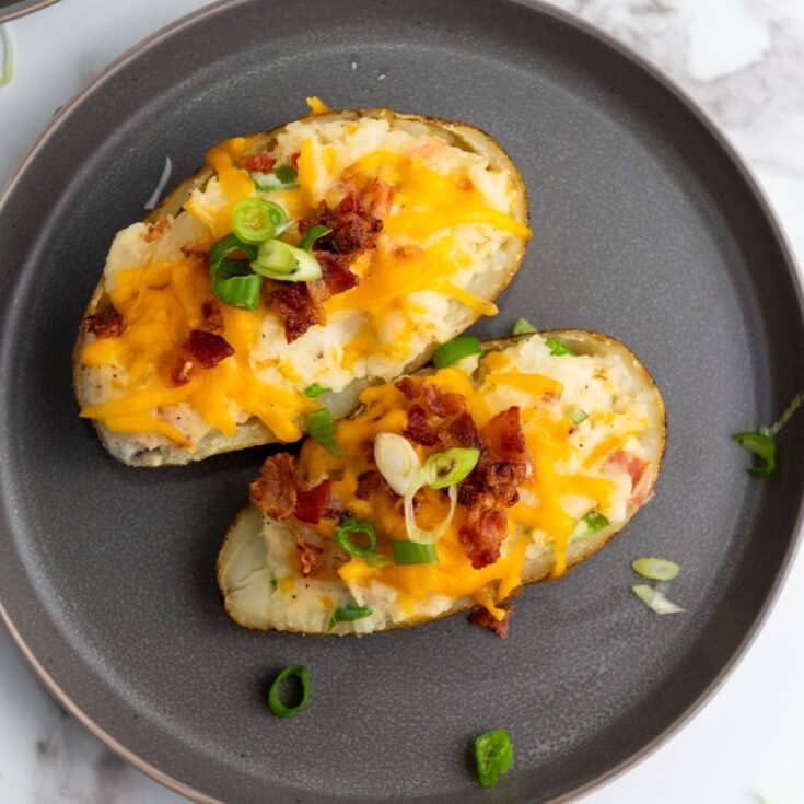 Two twice-baked potato halves served on a plate, topped with melted cheese, bacon bits, and sliced scallions.