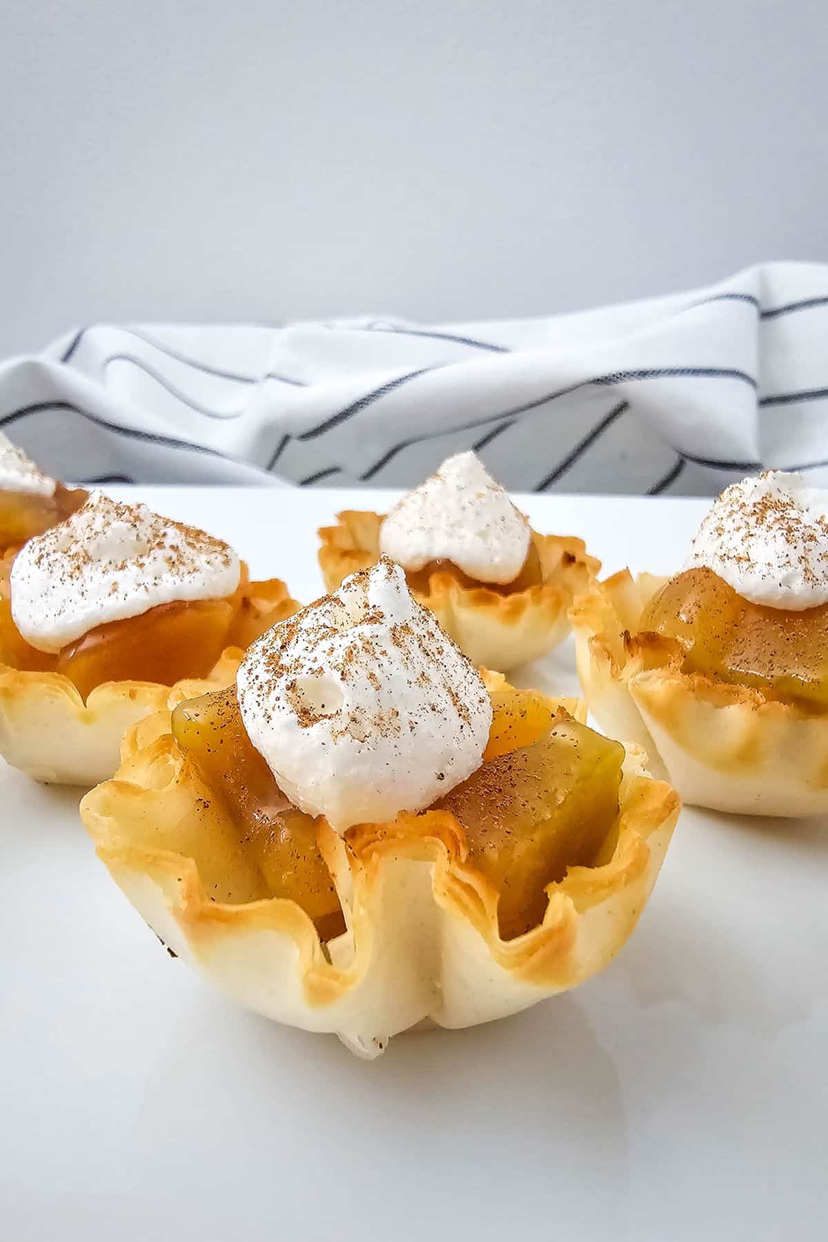Mini pie bites with peach filling and whipped cream, sitting in crispy phyllo shells.