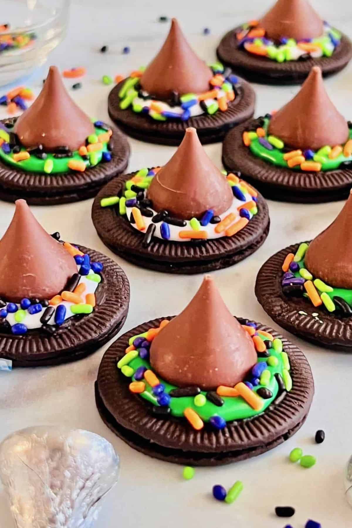 Witch hat cookies made with chocolate cookies, frosting, and chocolate kisses, displayed on a flat surface.