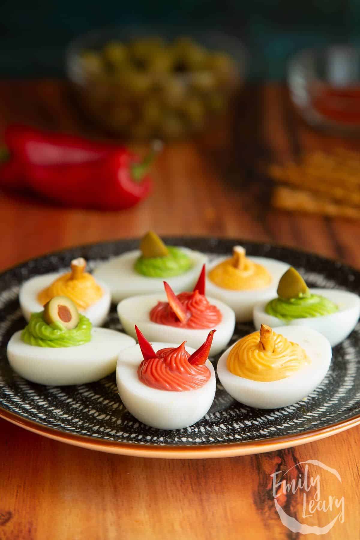 A plate filled with deviled eggs decorated with spooky toppings, styled with vibrant colors and Halloween-inspired details.