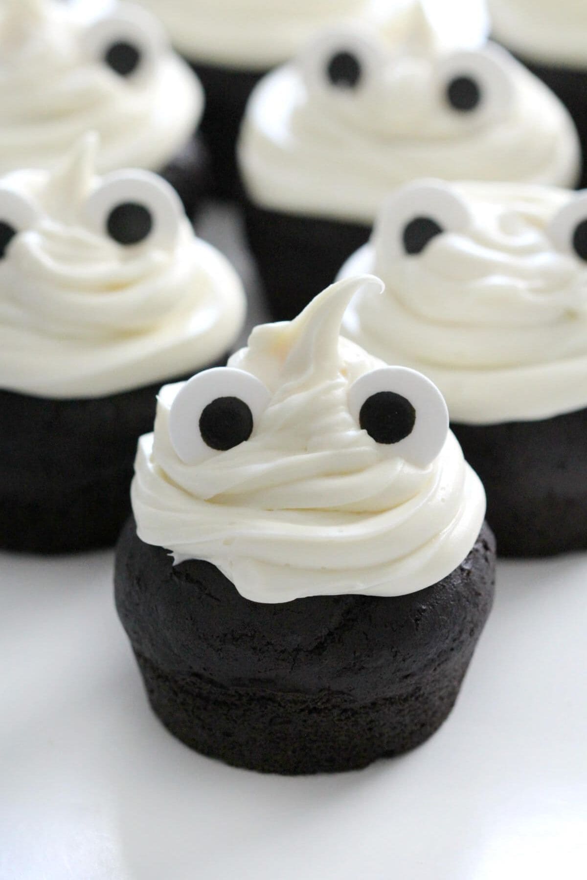 Close-up of ghost-shaped cupcakes topped with candy eyes and smooth white frosting.