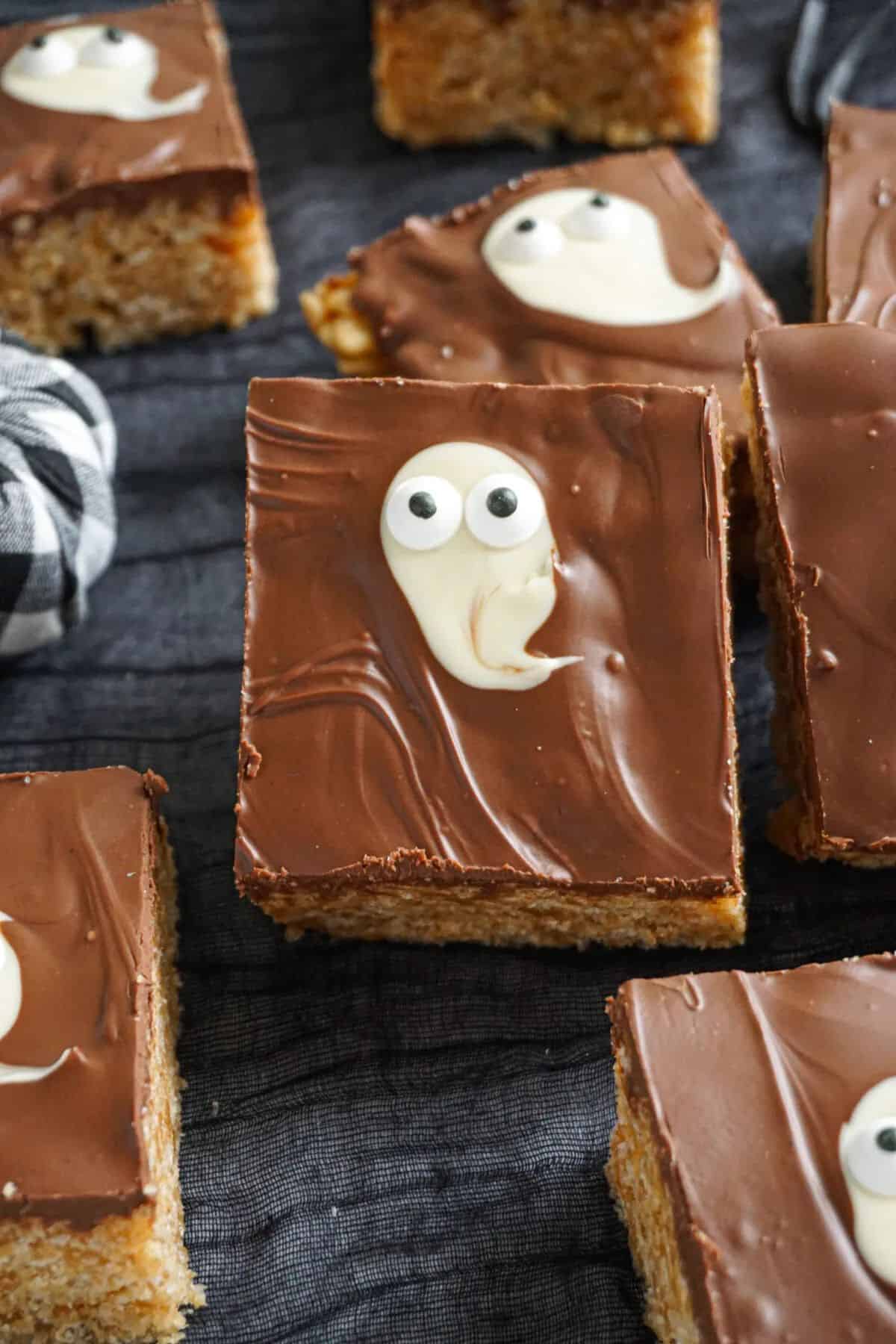 Close-up of Ghosteroos showing crispy rice cereal bars coated in chocolate and butterscotch, topped with white chocolate ghosts and candy eyes.