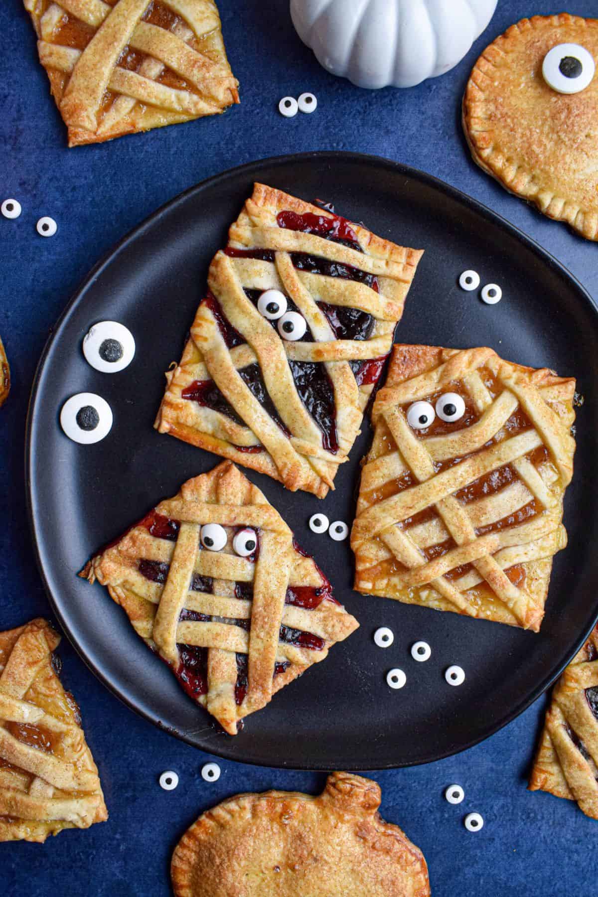 Flaky hand pies with candy eyes on a plate, with more pies blurred in the background.