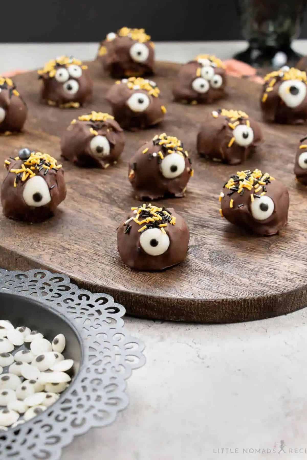 Monster pumpkin cheesecake truffles decorated with chocolate and candy details, arranged on a rustic wood board.
