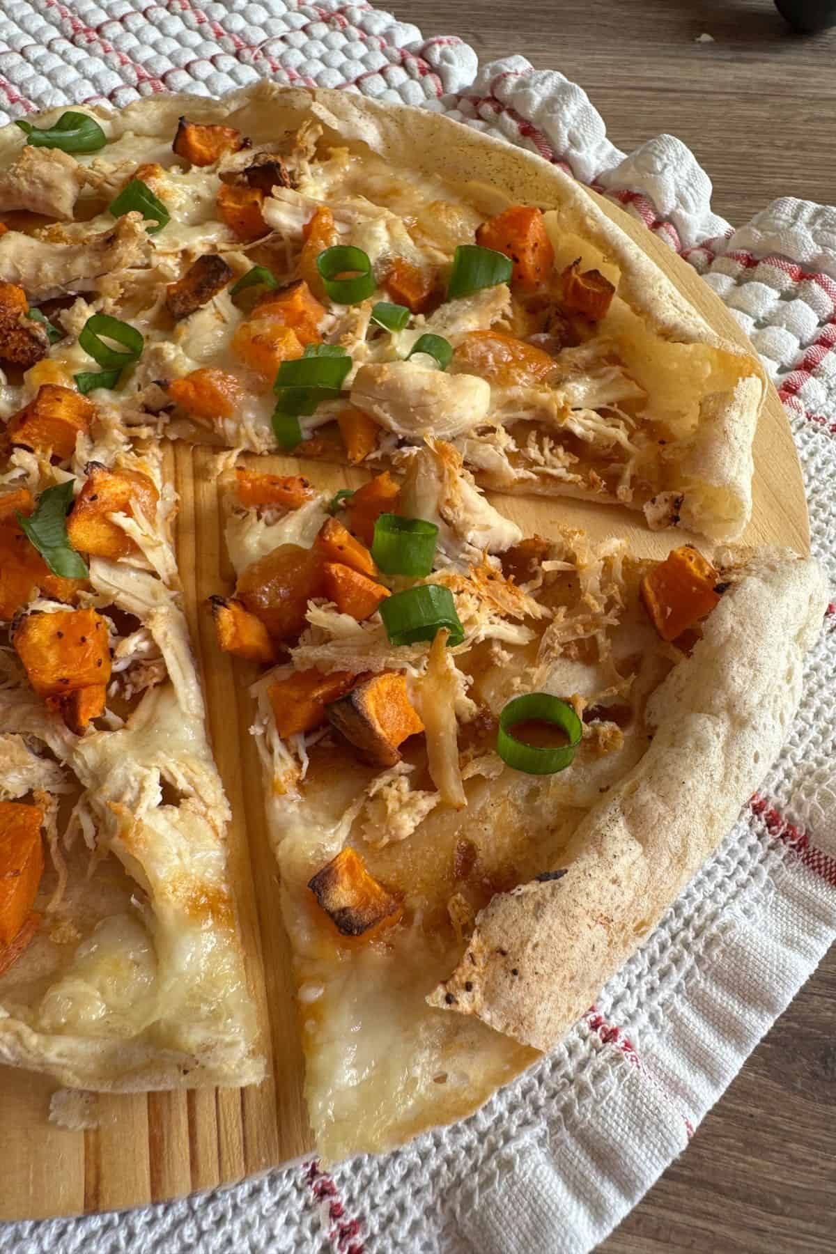 A sourdough pizza topped with chicken and sweet potato resting on a cloth.
