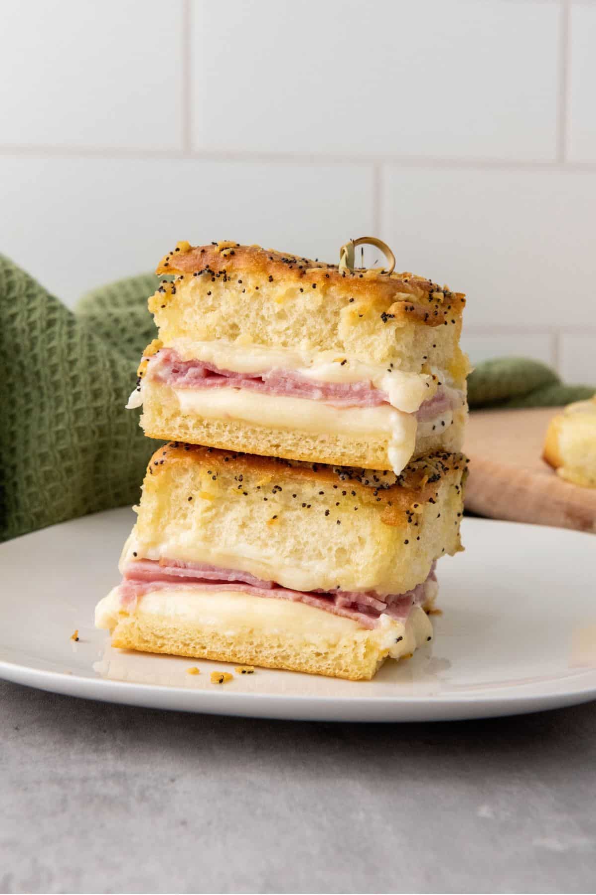 A plate with two layer of melty ham and cheese sliders showing its interior.