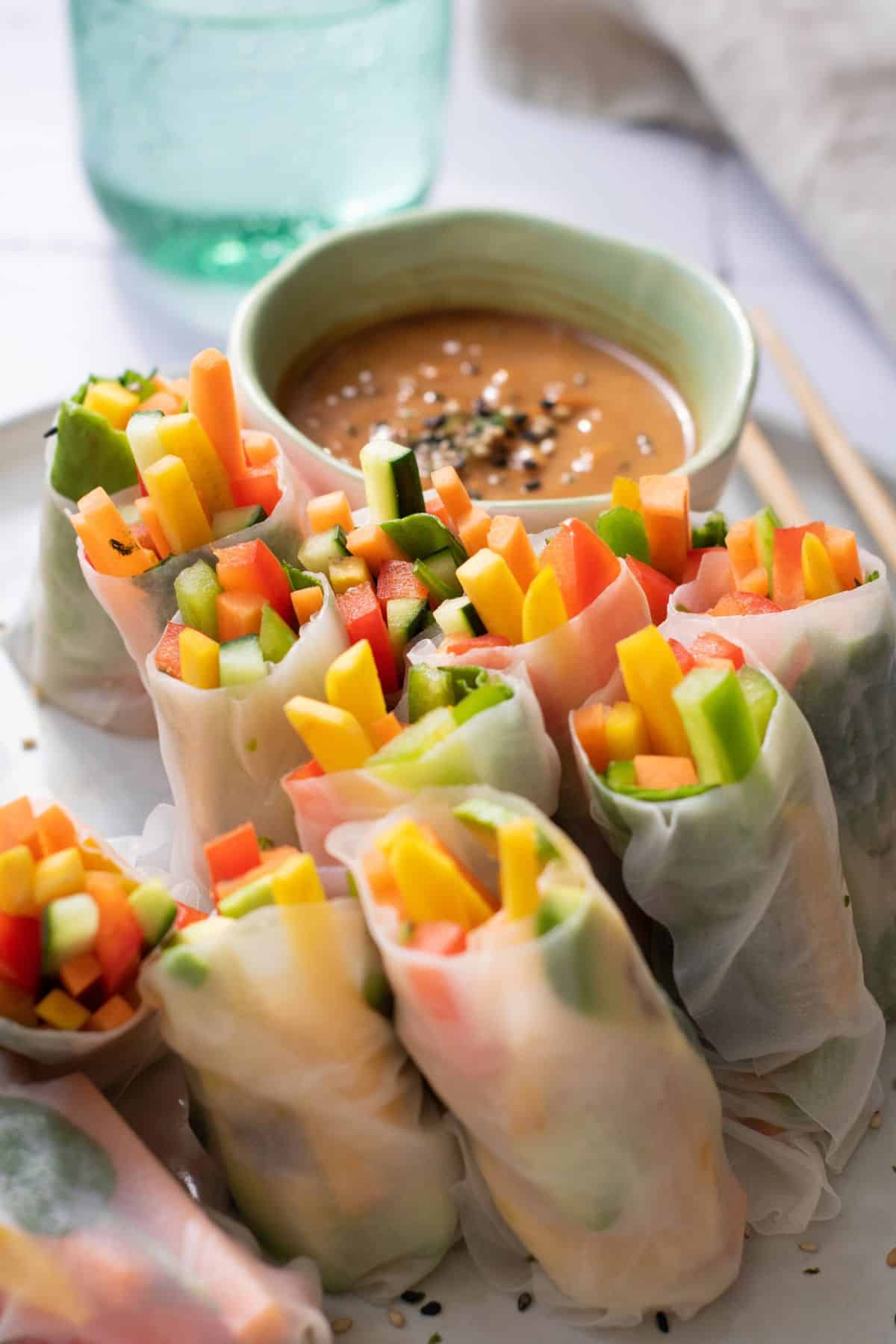 A plate with rainbow veggie rolls served with dipping sauce and chopstick placed on the side.