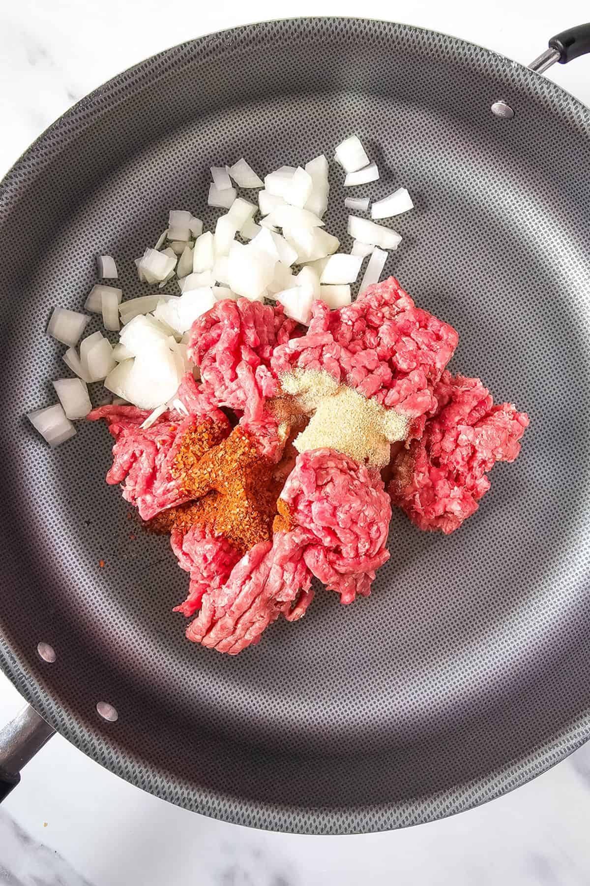 Seasoned ground beef and diced onion cooking in a medium pan.