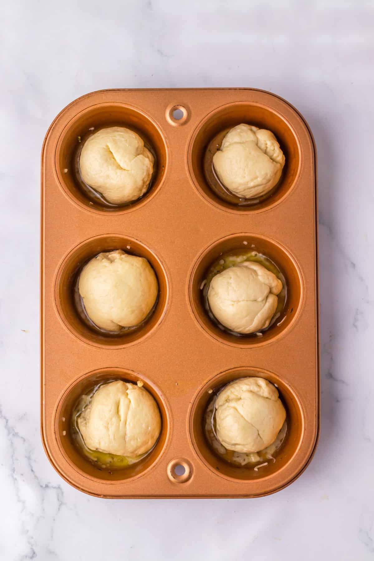 Pizza dough balls placed in a muffin tin.