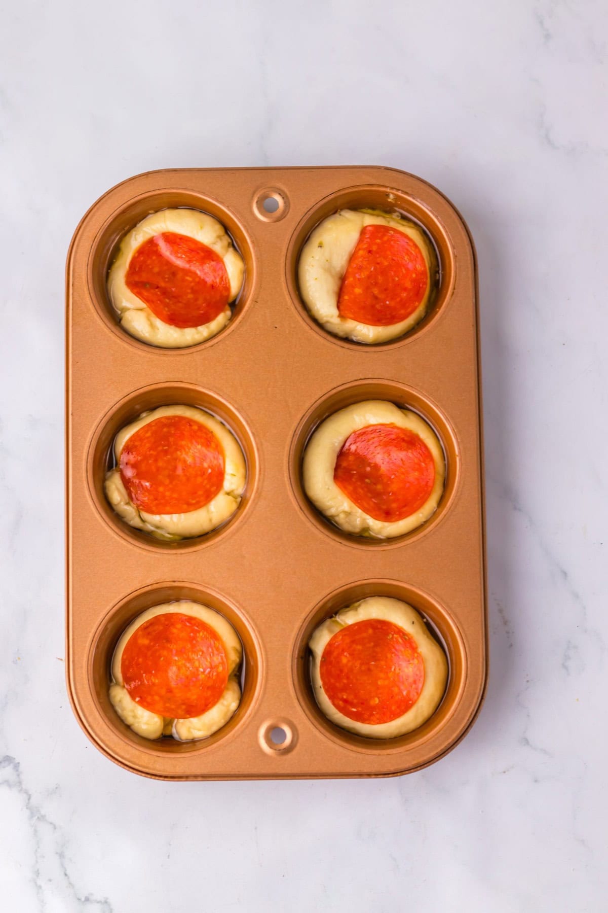 Pizza dough in muffin tin topped with red sauce.