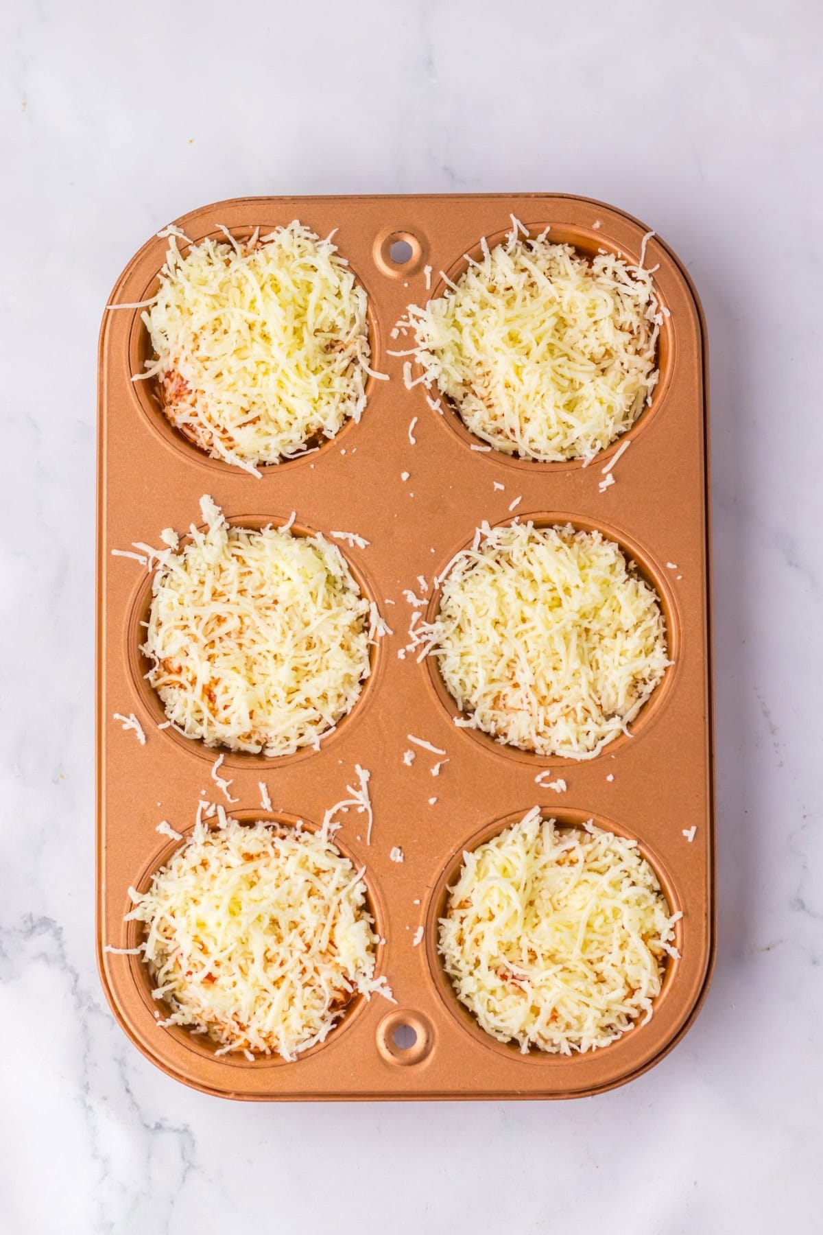 Baked pizza puffs in a muffin tin topped with overloaded cheese