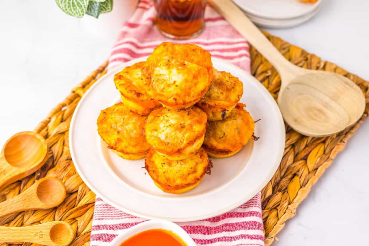Stack of cheesy muffin tin pizza puffs served on a white plate.