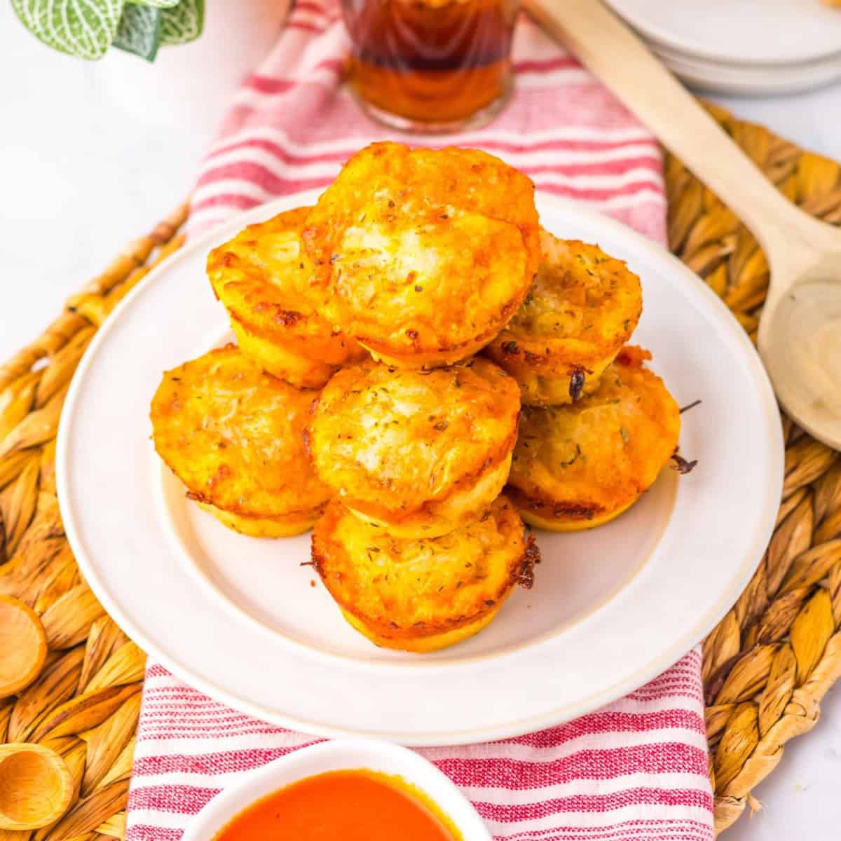 Stack of cheesy muffin tin pizza puffs served on a white plate.