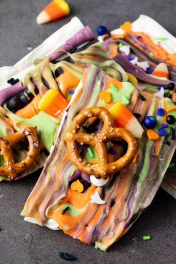 Finished Halloween candy bark set on a flat surface, topped with colorful swirls of melted candy, candy corns, pretzel pieces, and festive sprinkles.