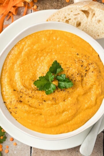 A bowl of creamy soup with garlic bread resting on it.