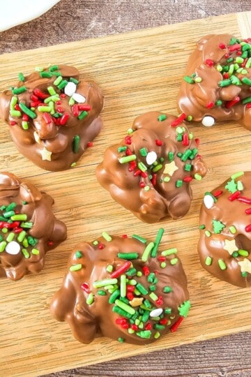 Chocolate crockpot candies arranged on a wooden board, topped with Christmas sprinkles.