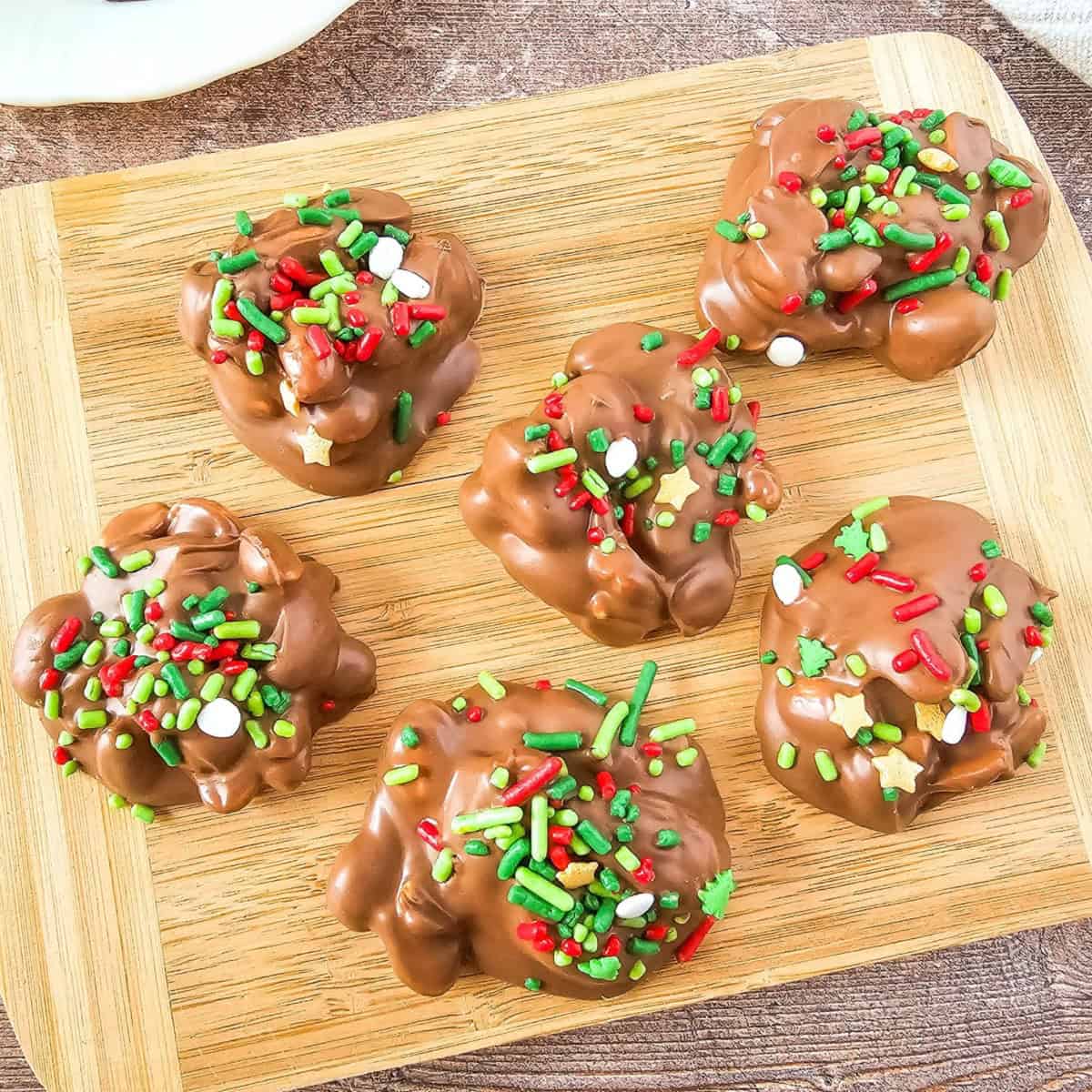 Chocolate crockpot candies arranged on a wooden board, topped with Christmas sprinkles.