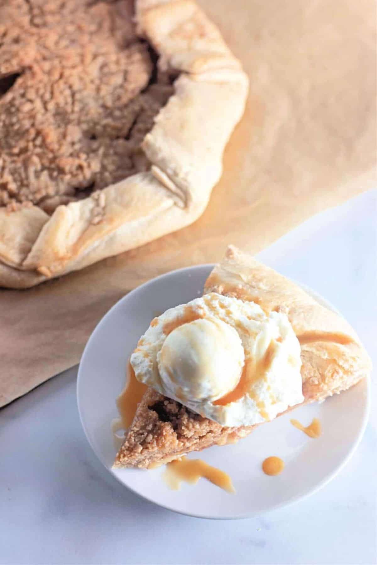 Slice of apple galette with crumb topping served on a plate, topped with a scoop of vanilla ice cream.