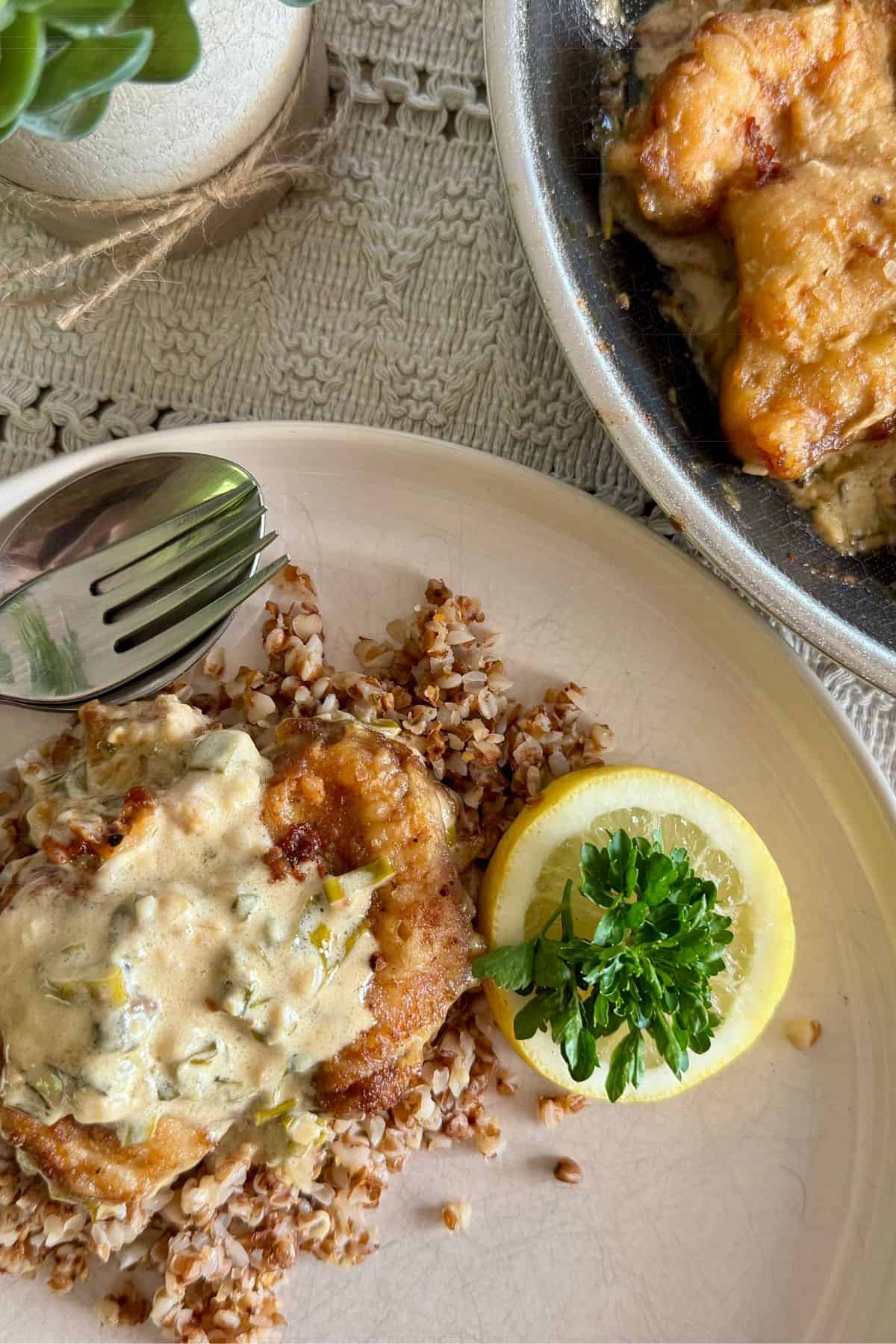 A plate with creamy lemon chicken thighs with dijon and parsley served with lemon.