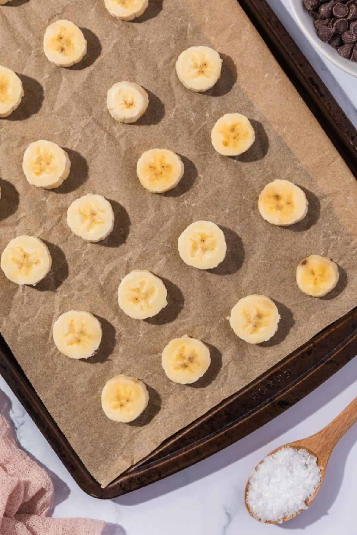 Sliced banana pieces lined up evenly in a baking pan lined with parchment paper.