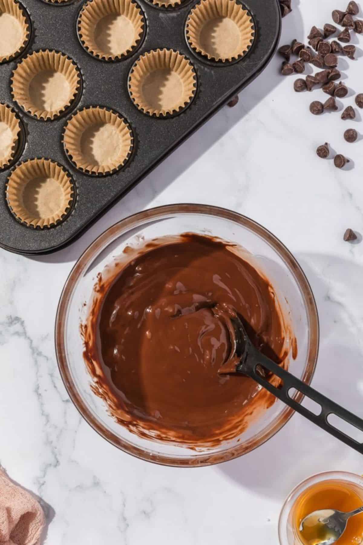Chocolate kisses melting in a bowl with a spatula resting on it.